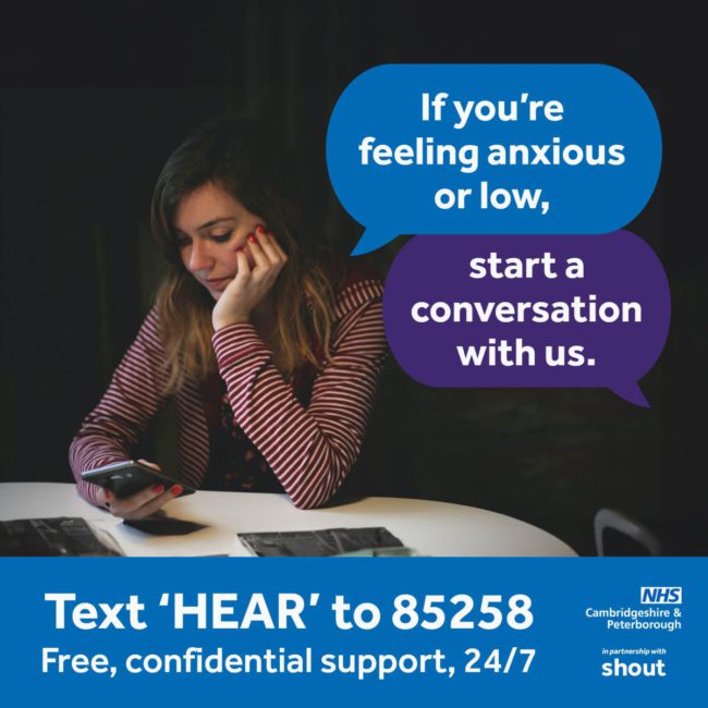 img94joktmu78493 Woman using her phone in a dark room. Text bubbles say: If you're feeling anxious or low, start a conversation with us. White text on a blue banner reads: Text HEAR to 85258 Free confidential support 24/7. NHS Peterborough and Cambridgeshire, and in partnership with shout logos are on the bottom right corner.